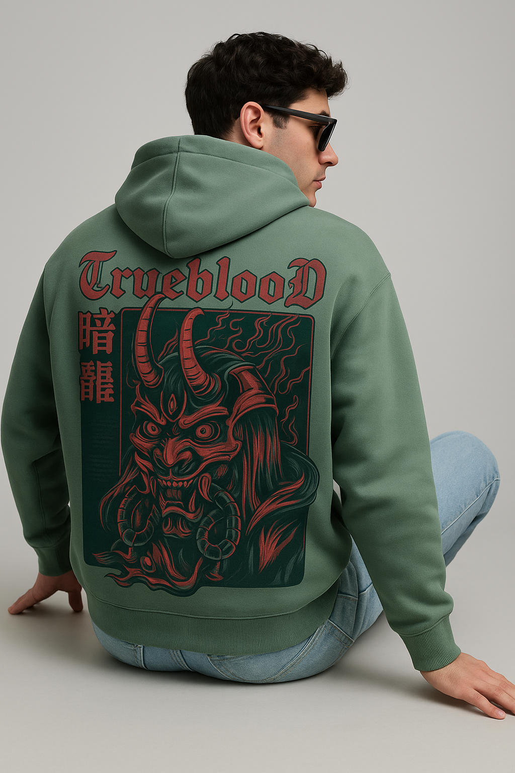 Oversized sage green hoodie with a red and black demon mask graphic on the back.